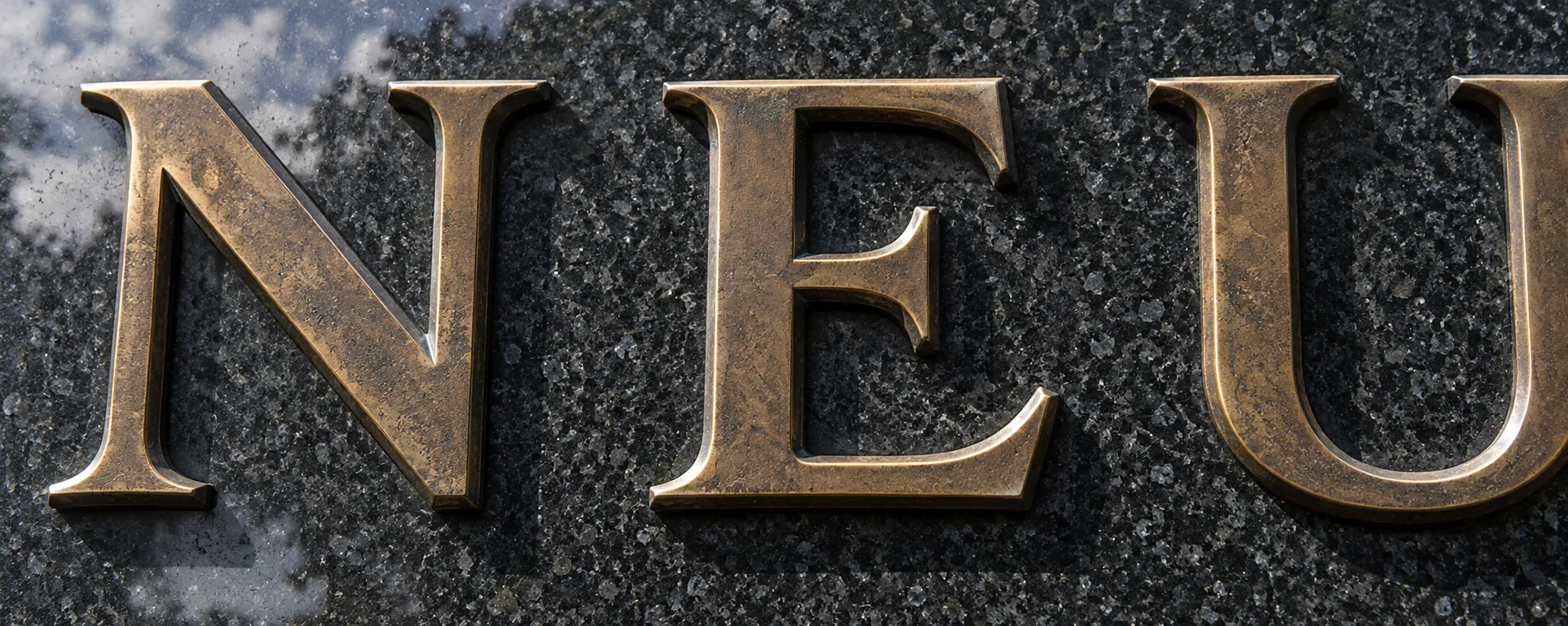 Aufgesetzte Buchstaben aus Bronze auf dunklem, poliertem Granit